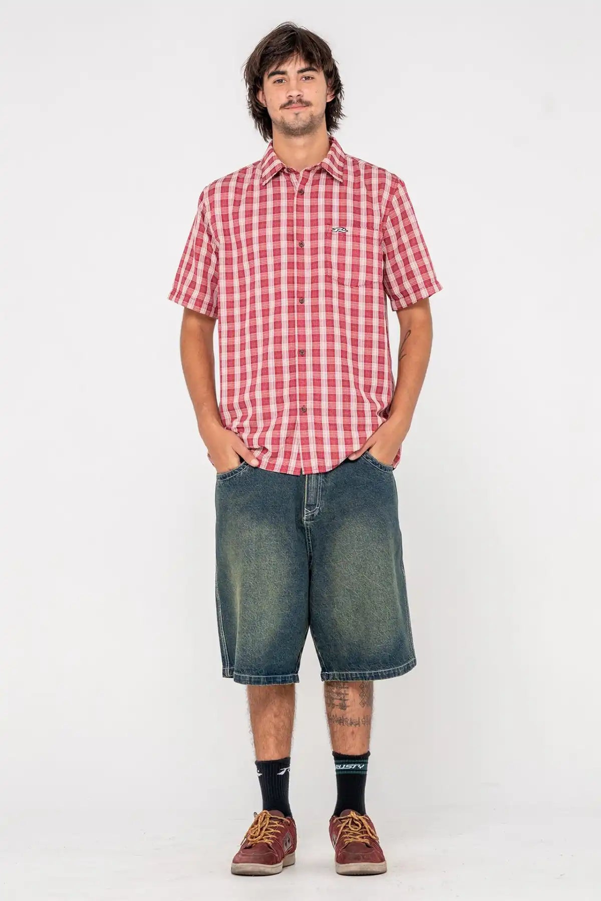 Person wearing a Rusty red and white checkered shirt and blue denim shorts on a white background