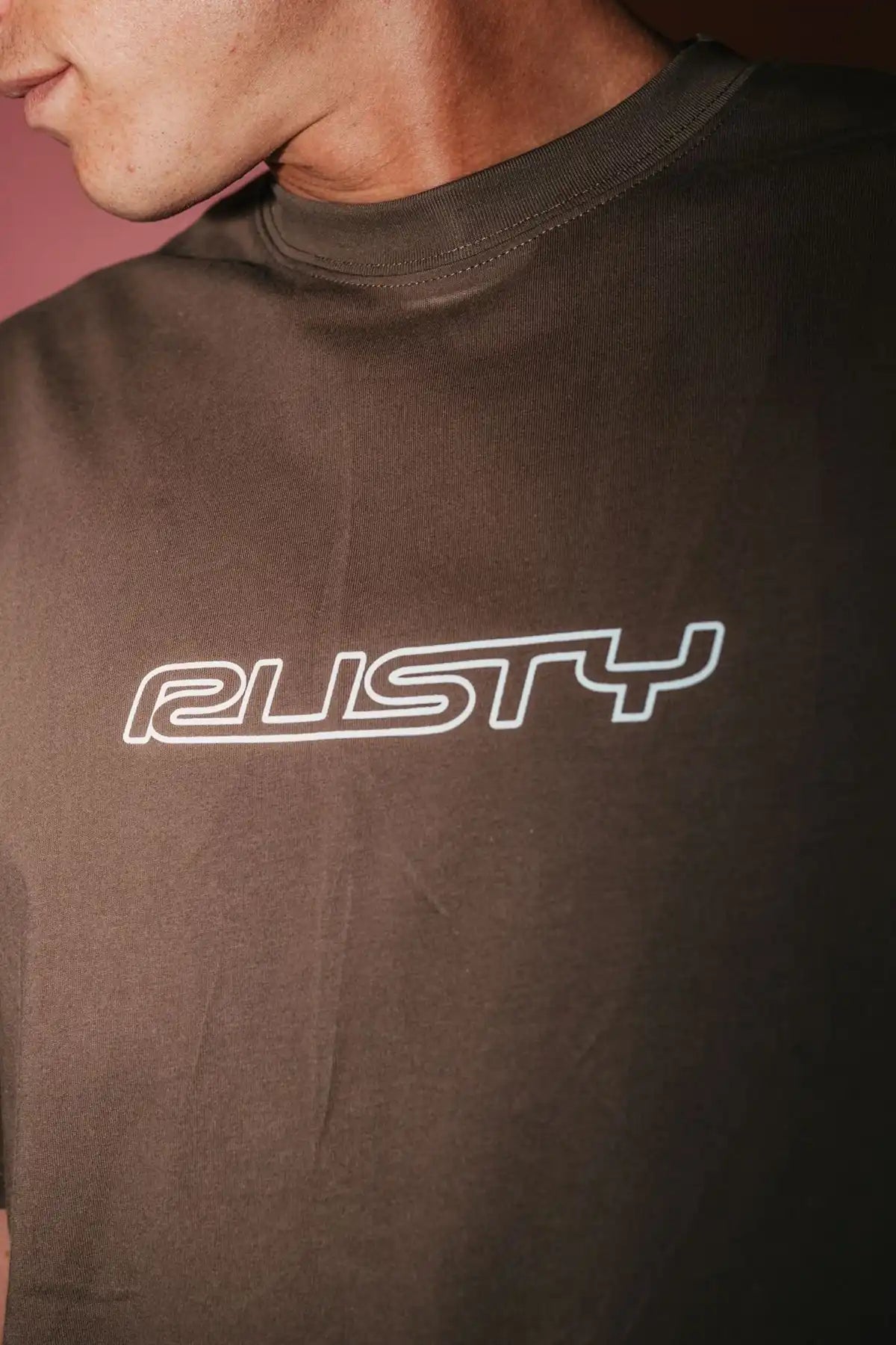 Person wearing a brown t-shirt with 'RUSTY' logo