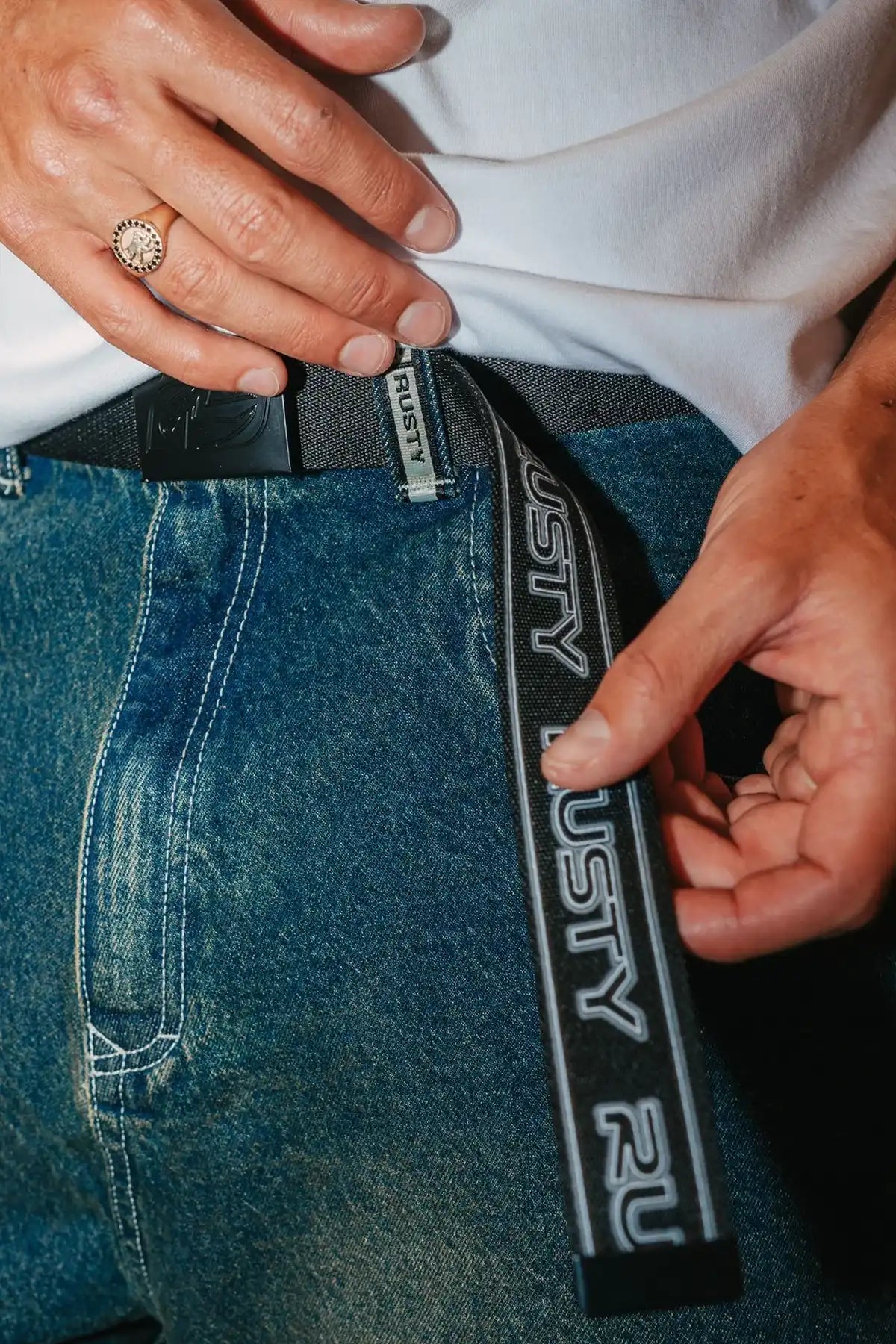 man wearing a Rusty Jagged Webbing Belt — Black showing the side with the rusty logo