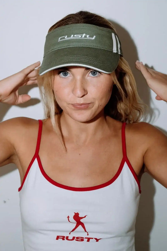Woman wearing a white tank top with a red logo and a Rusty Love Visor in Arm Green with 'Rusty' branding.
