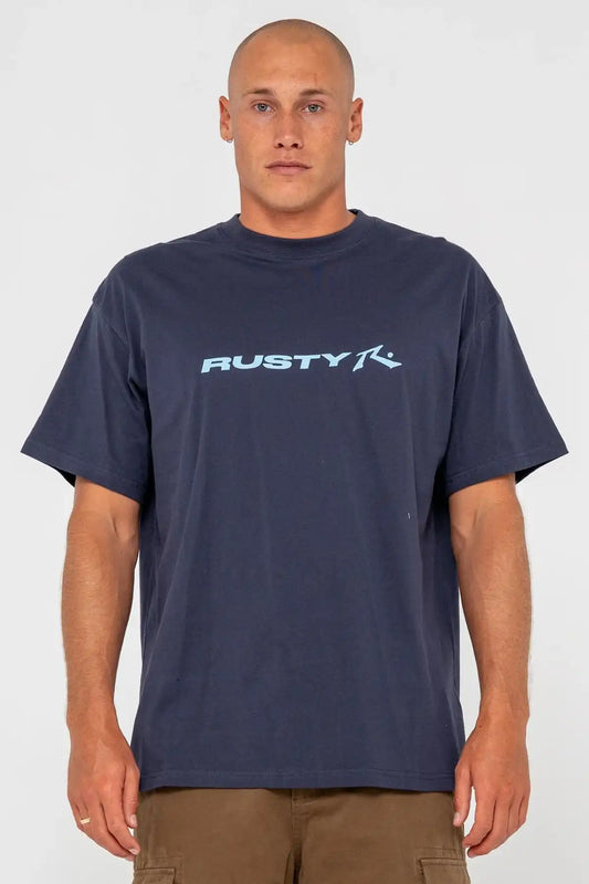 Man wearing a Rusty Mens Vital Rusty Graphic Tee in Navy with large logo on the front and pinecone short against white background