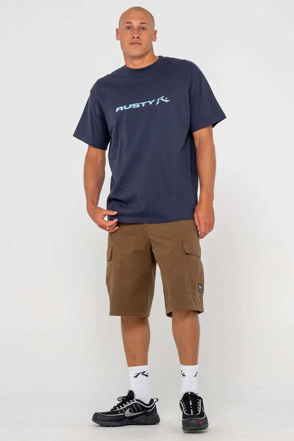Man wearing a Rusty Mens Vital Rusty Graphic Tee in Navy with large logo on the front and pinecone short against white background