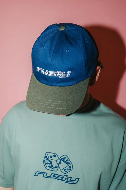 Person wearing a Rusty Rusty Road Trip Dad Cap in Navy Blue with 'Rusty' branding against a pink background