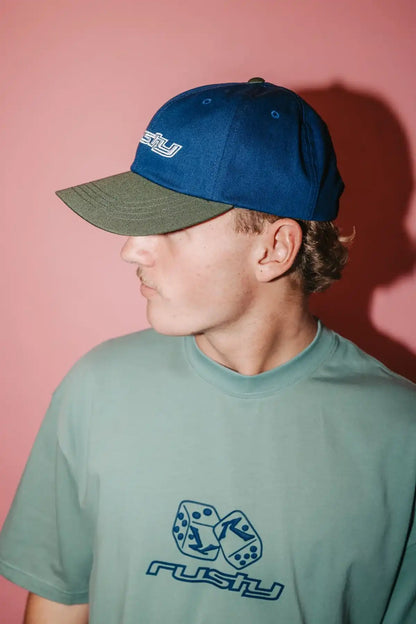 Person wearing a Rusty Rusty Road Trip Dad Cap in Navy Blue and matching t-shirt with 'Rusty' logo against a pink background