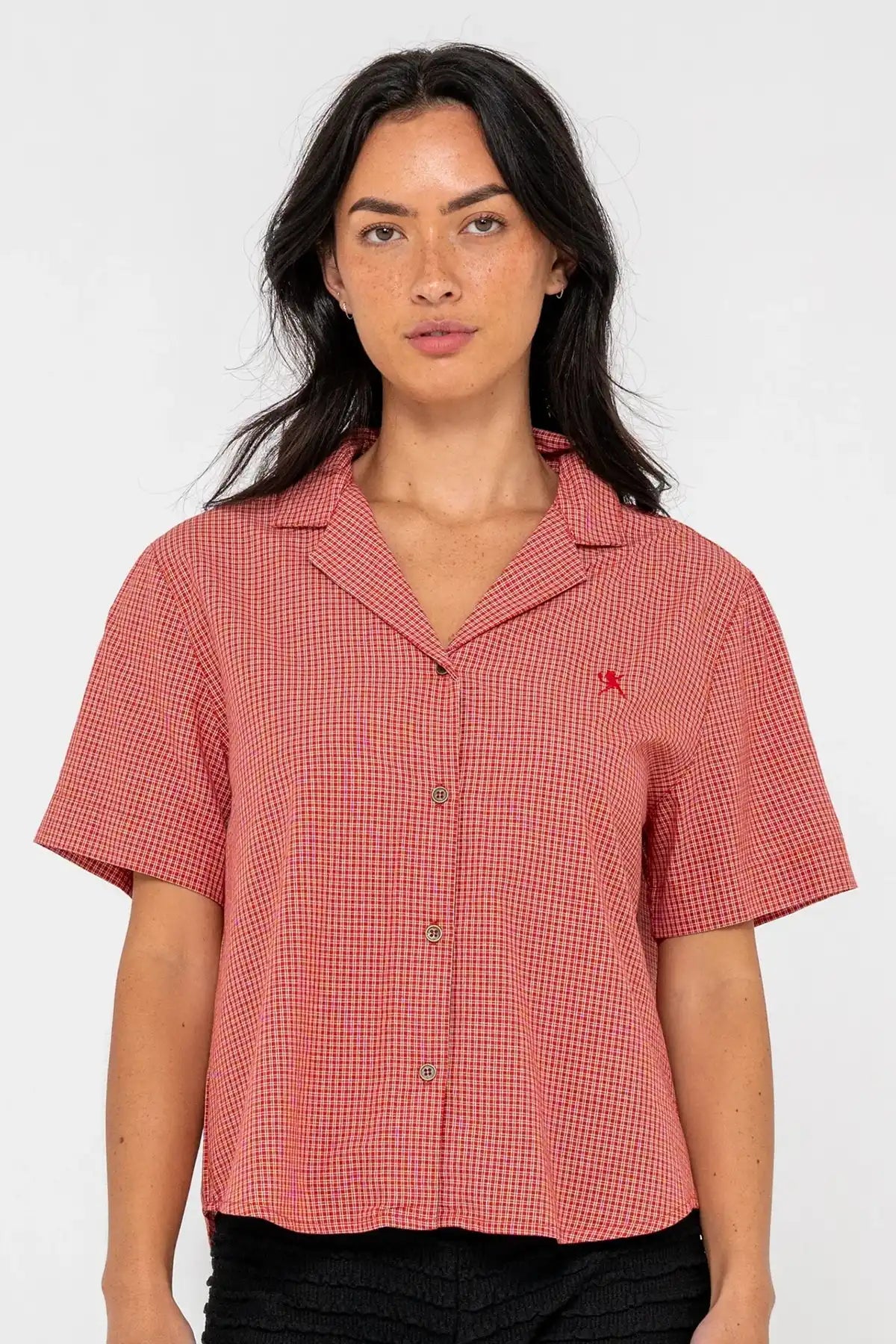 woman wearing Rusty Summer Court red Boxy Shirt and black shorts on a pink background front on view