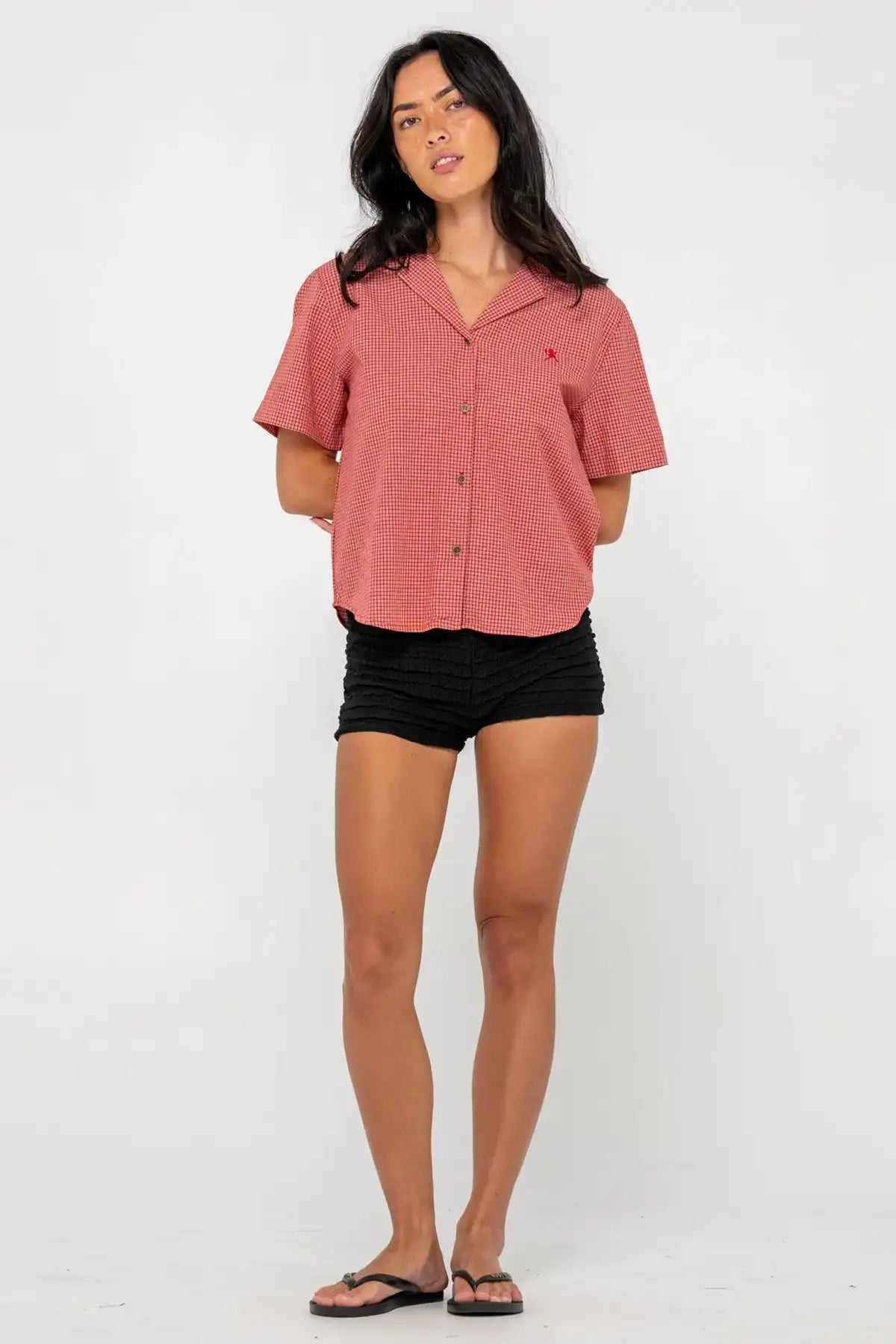 woman wearing Rusty Summer Court red Boxy Shirt and black shorts on a pink background full model view