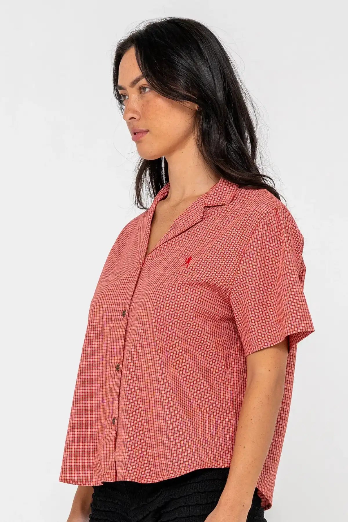woman wearing Rusty Summer Court red Boxy Shirt and black shorts on a pink background side view