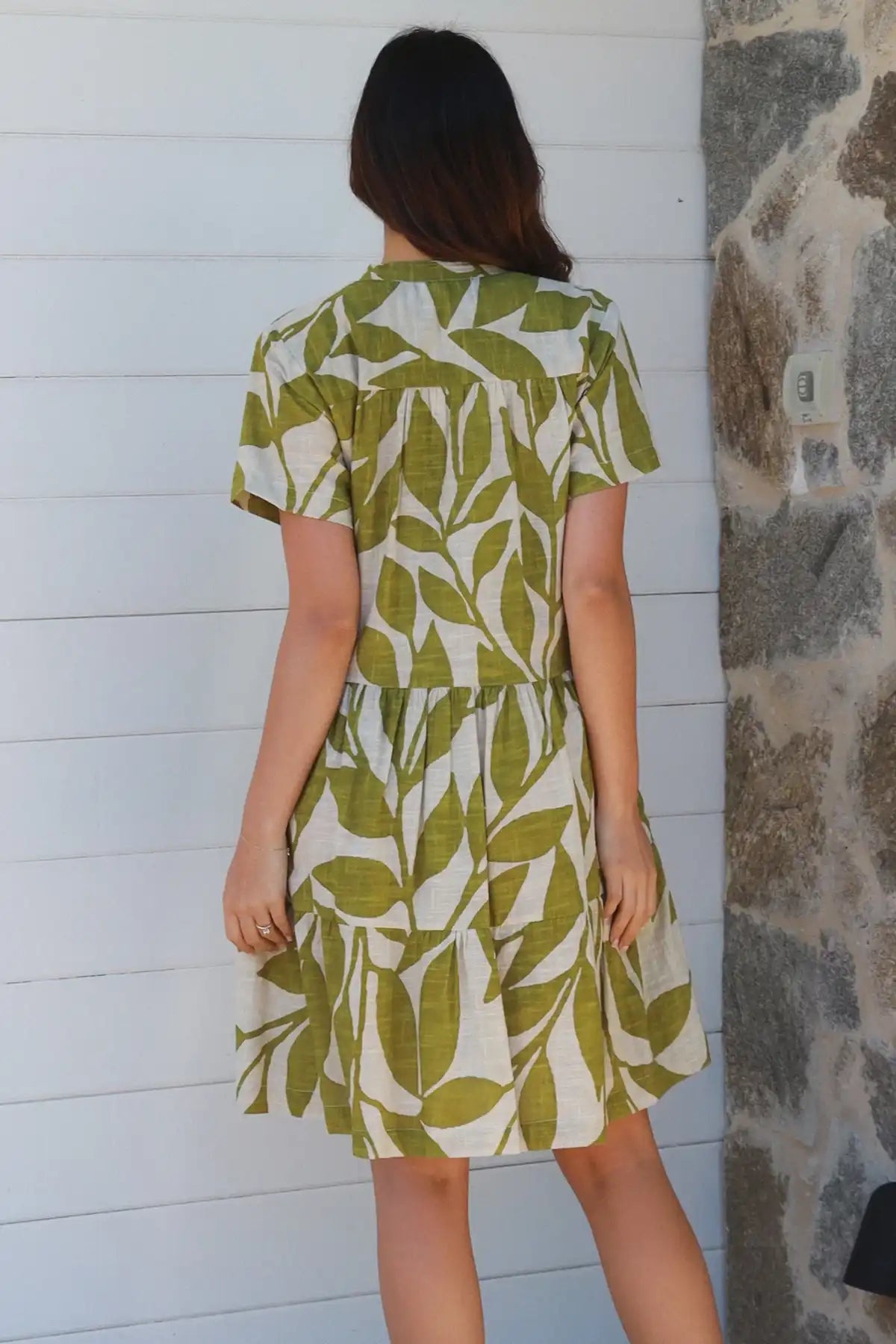 Woman wearing a green and white leaf-patterned dress against a white wall.