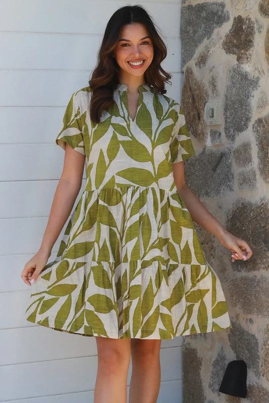 Woman wearing a green and white leaf-patterned dress standing against a stone wall.