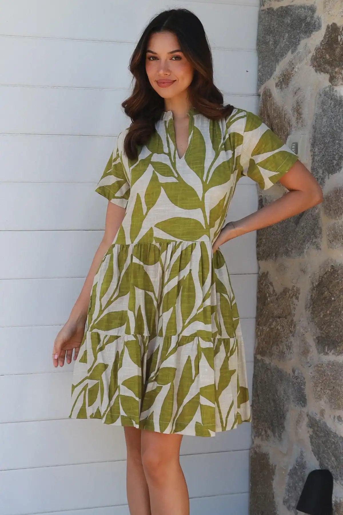 Woman wearing a green and white leaf-patterned dress against a white wall and stone column.