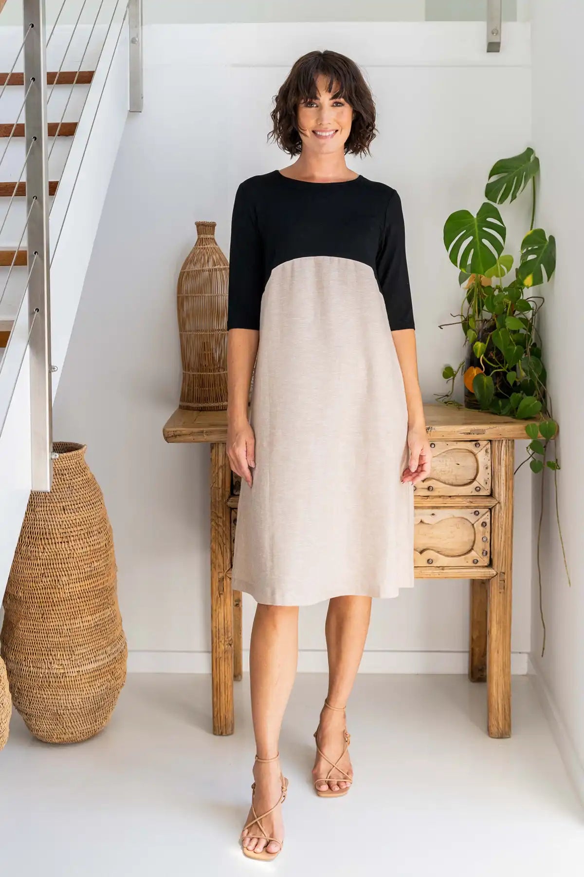 Woman wearing a See Saw Colour-Block Linen–Rayon Jersey Dress in Black/Natural standing front on in a home setting with plants and furniture.
