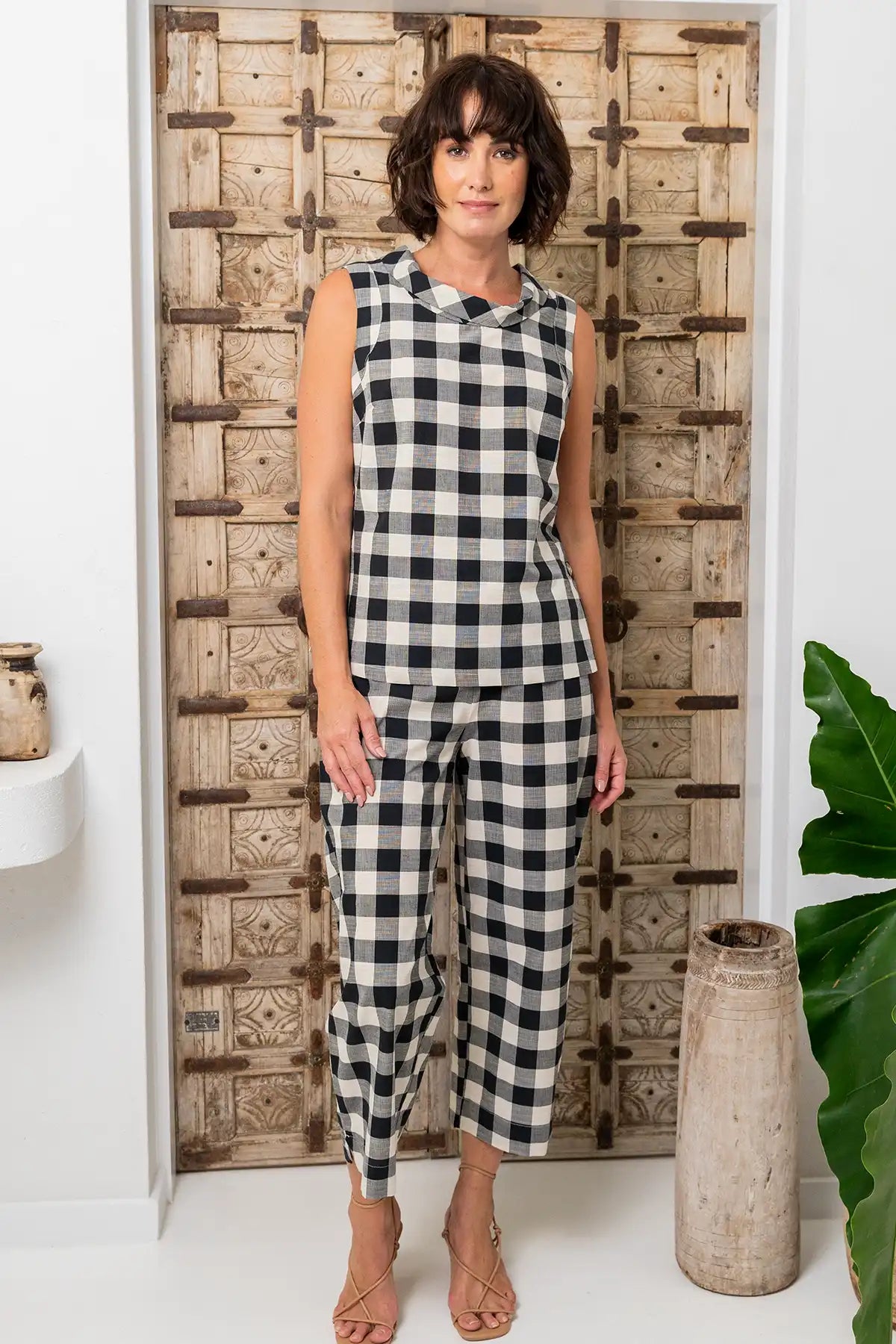 Woman wearing a See Saw Cotton Gingham Cowl Neck Top & pants in  Black/Natural standing in front of a wooden panel.