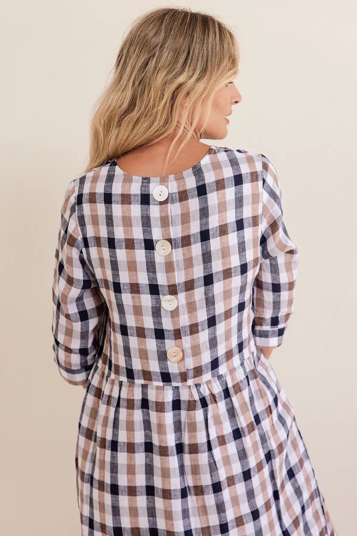 Woman wearing a plaid dress with buttons on a beige background
