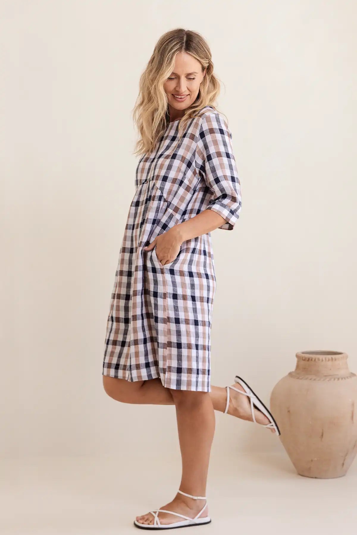 Woman wearing a plaid dress standing next to a ceramic vase on a plain background