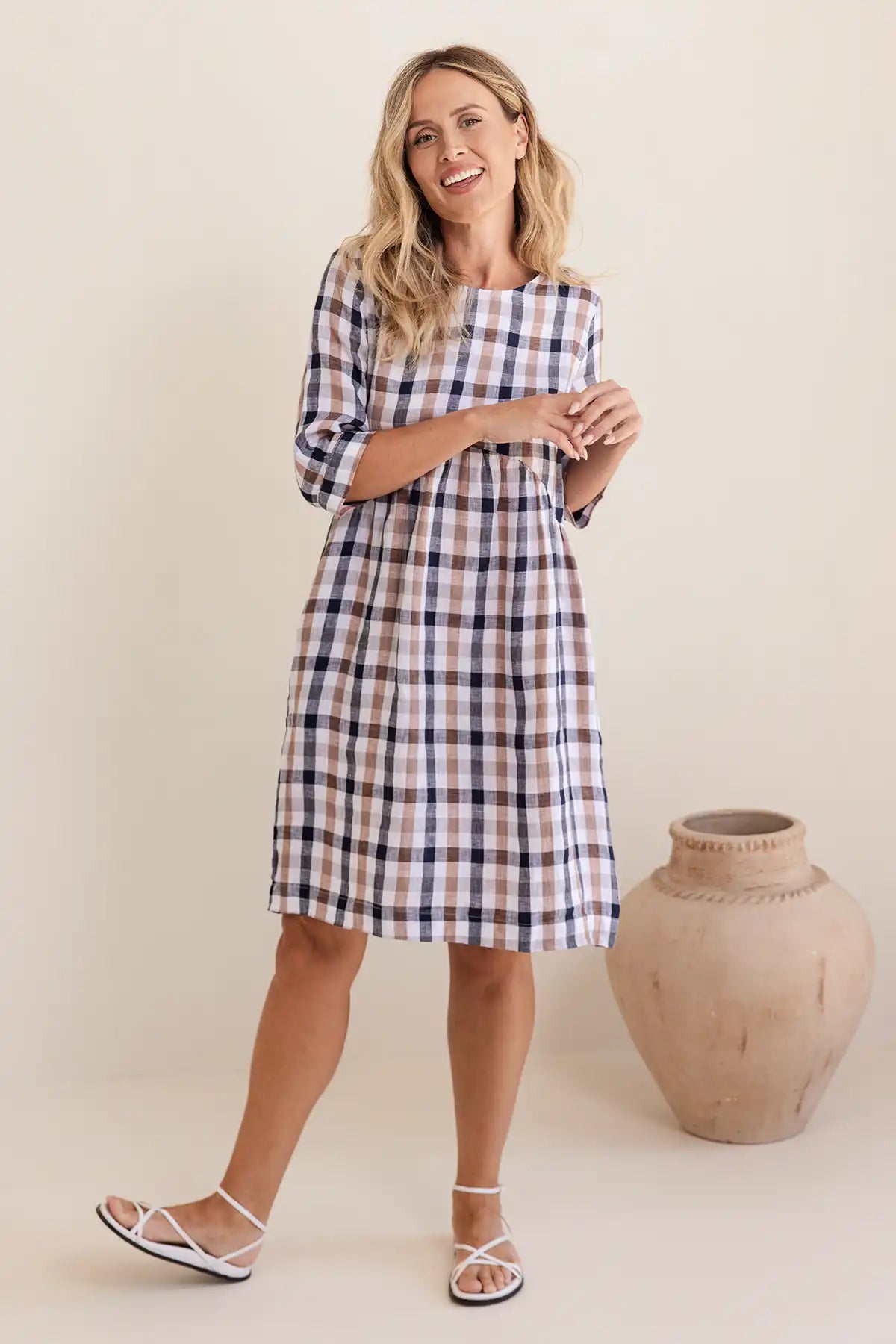 Woman wearing a plaid dress standing next to a large vase against a plain background