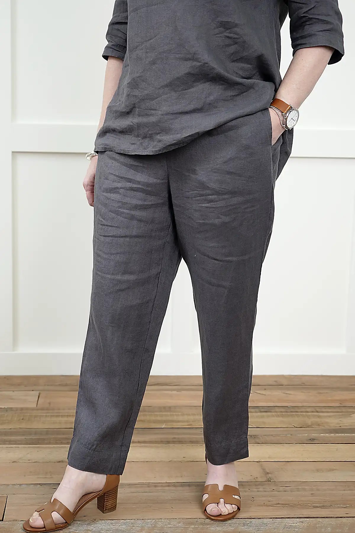 Person wearing a See Saw Linen 7/8 Flat Front Pant and cowl neck top in Charcoal on a wooden floor - 3/4 detail view of pants.