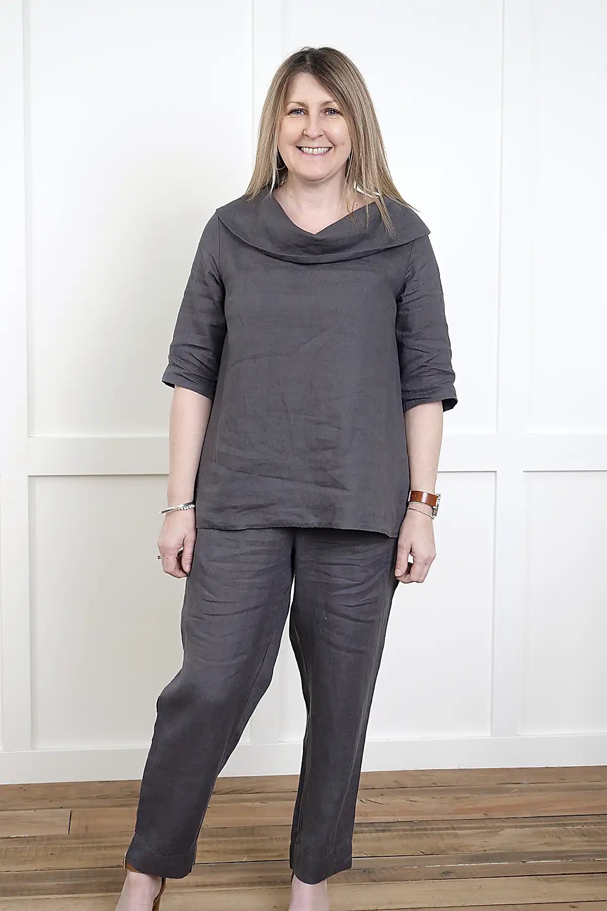 Woman wearing a See Saw Linen 7/8 Flat Front Pant and cowl neck top in Charcoal standing against a white wall.