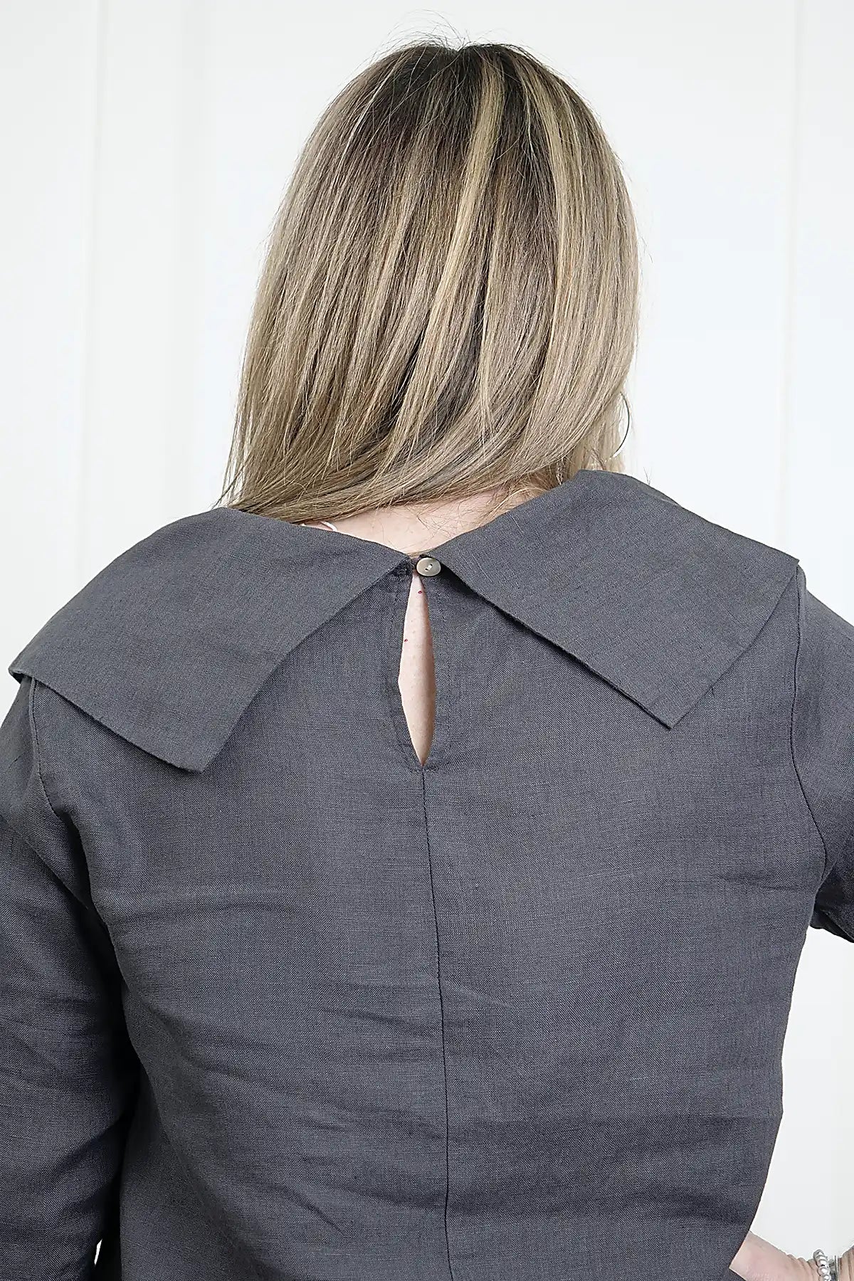 Person wearing a See Saw Linen Cowl Neck Top in Charcoal showing the detail of the cowl and buttron closure at the back of the top against a white background