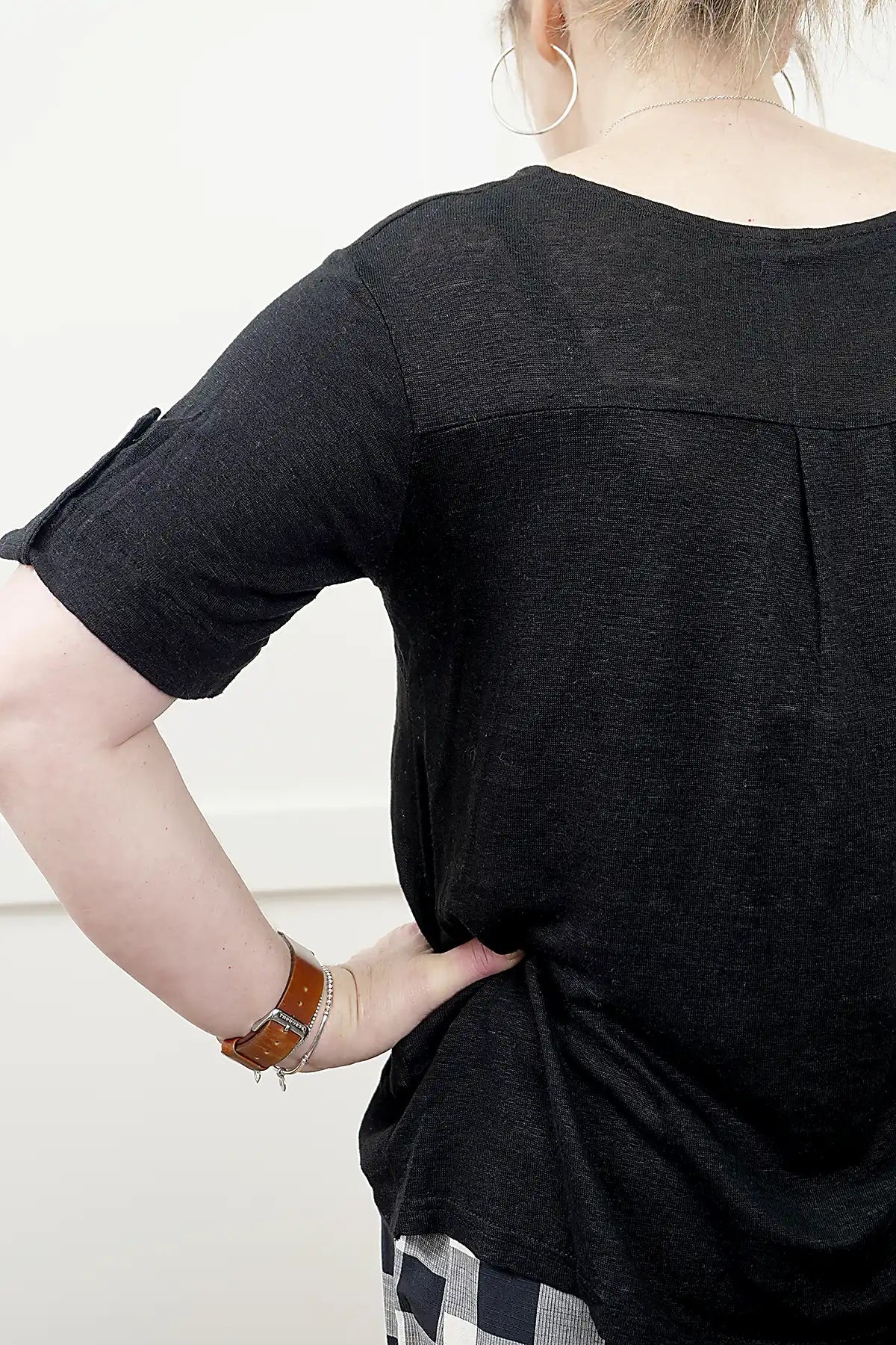 Person wearing a See Saw Linen Mixed Texture Top in Black detailed view of the back panels and sleeve with a plain background