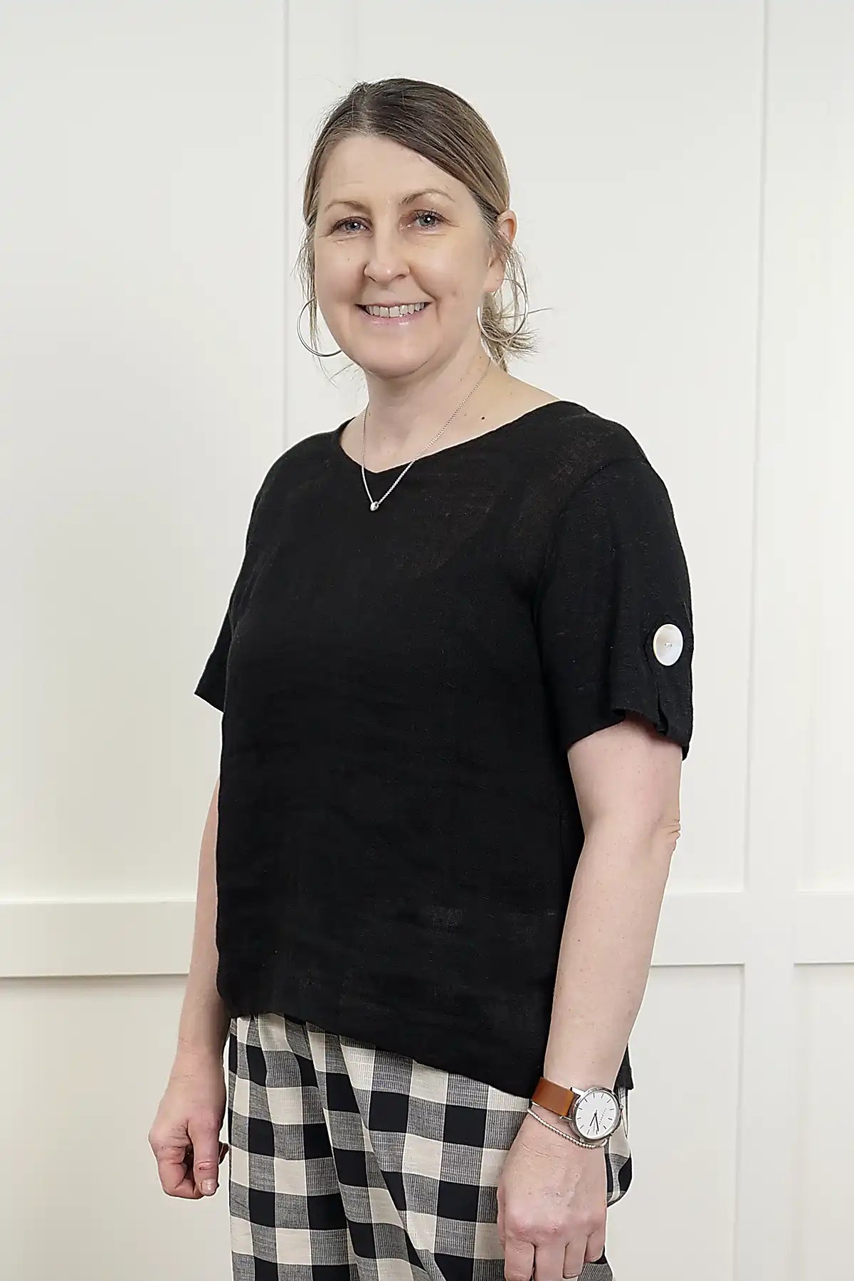 Woman wearing a See Saw Linen Mixed Texture Top in Black from side view and checkered pants against a white background
