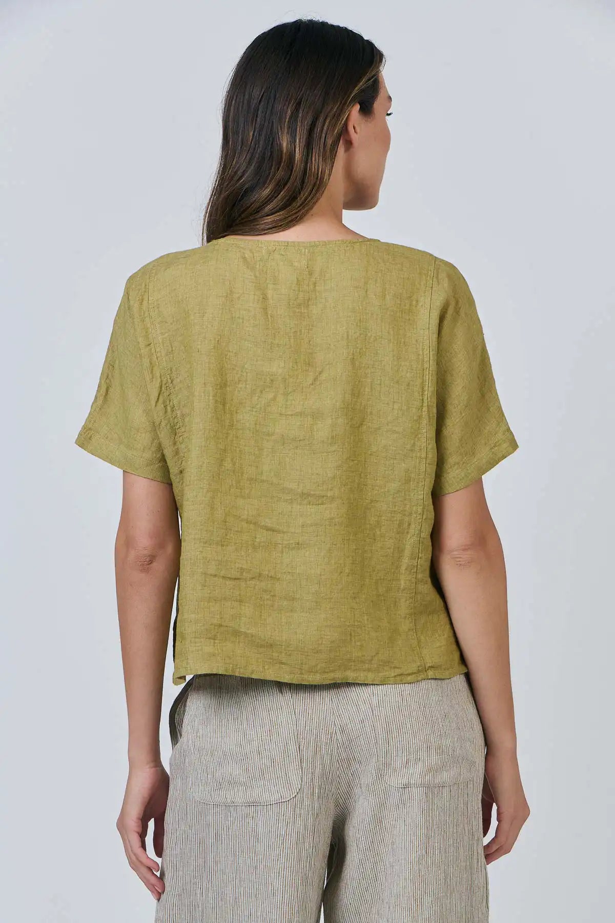 Woman wearing a Solace Linen Top in green Bamboo and beige pants against a white background back detiled view