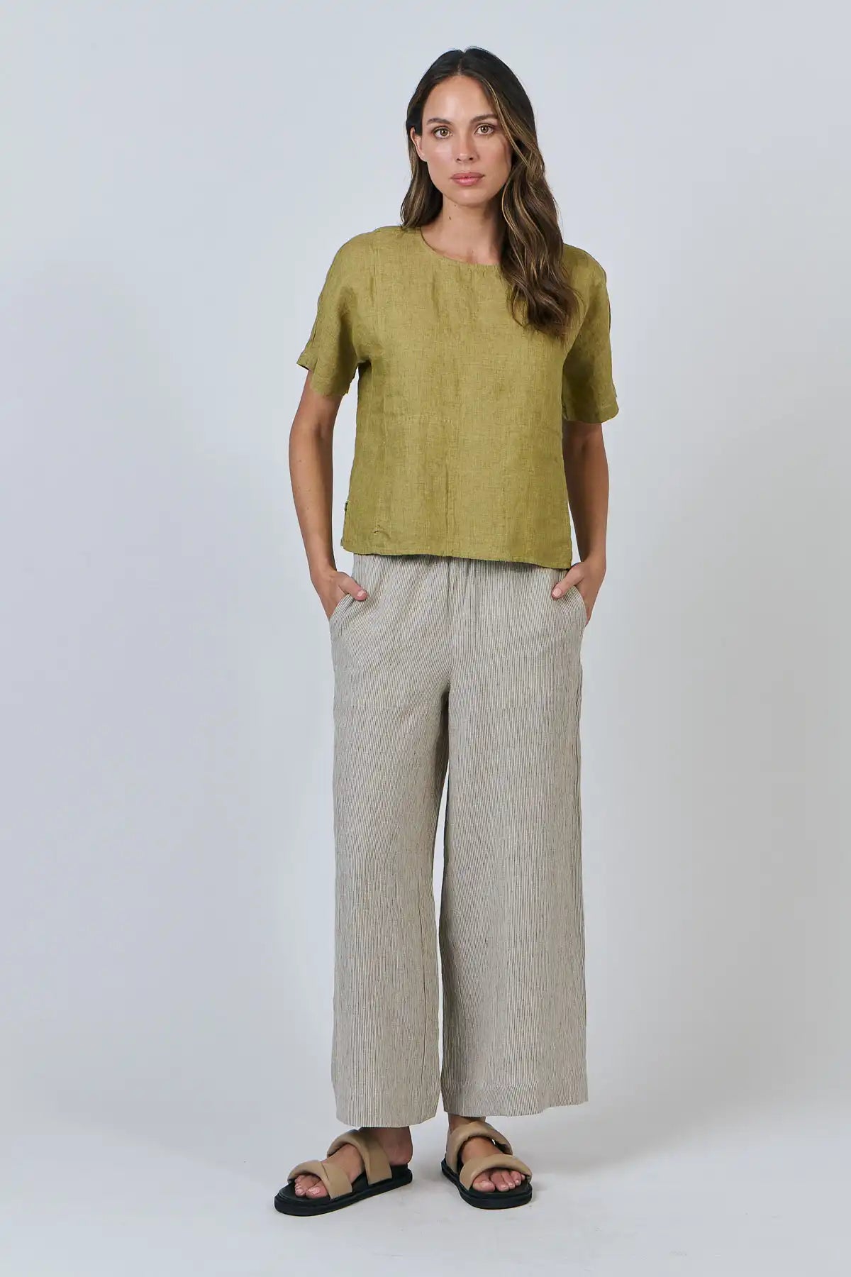 Woman wearing a Solace Linen Top in green Bamboo and beige pants on a white background front full model view