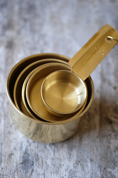 A set of nested brass measuring cups with long handles, arranged on a rustic gray wooden surface.