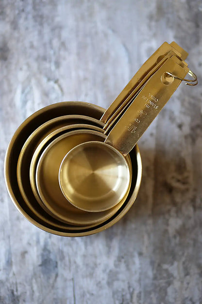 A set of nested brass measuring cups with handles, arranged diagonally on a textured gray stone surface.