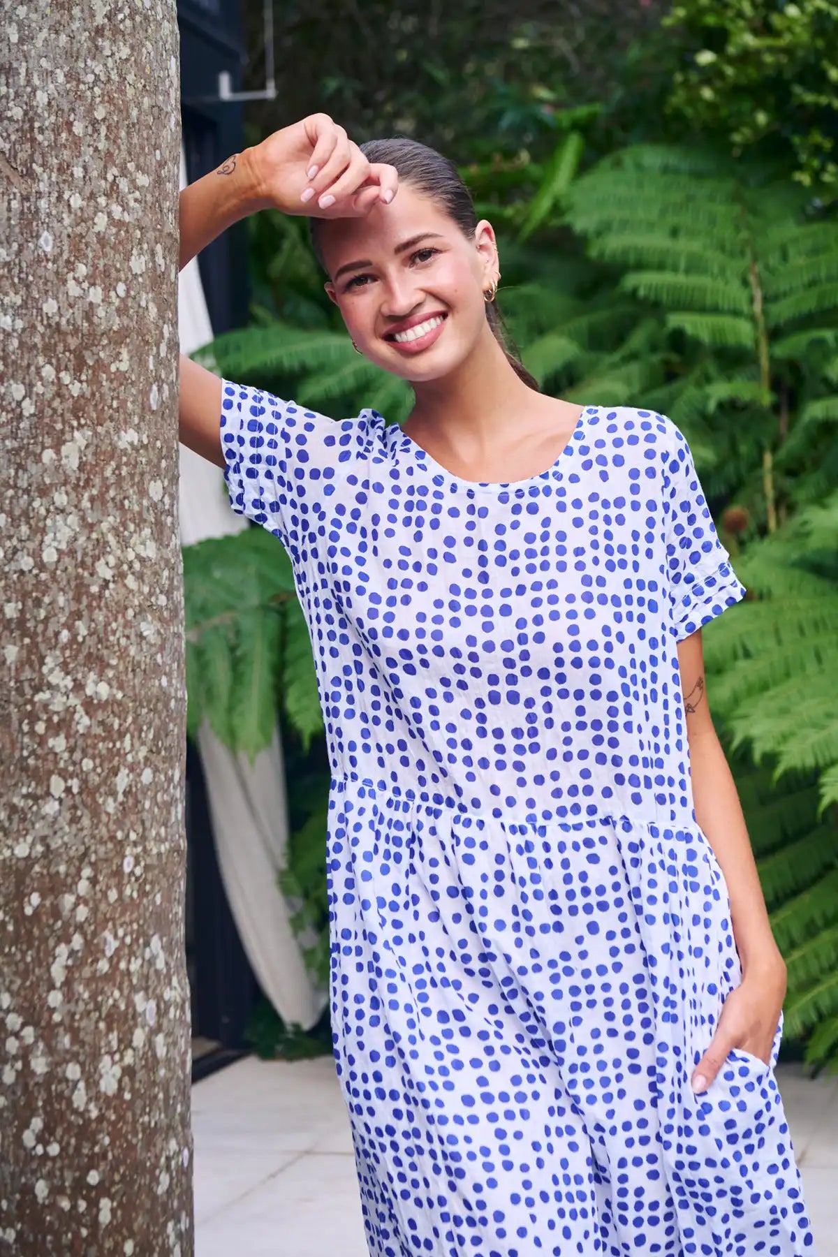 woman leaning on a tree in the garden wearing a white dress with blue dot print