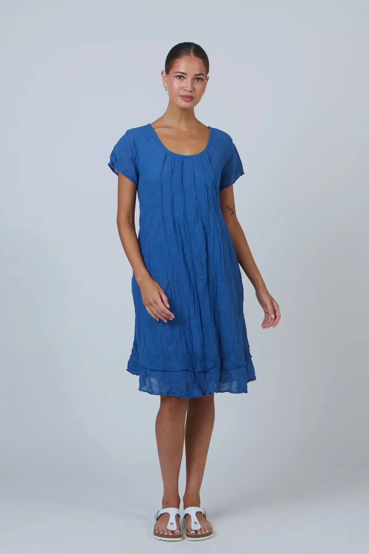woman wearing the Tidal Pleat Cotton Dress in Ocean Blue against a white background with white sandals