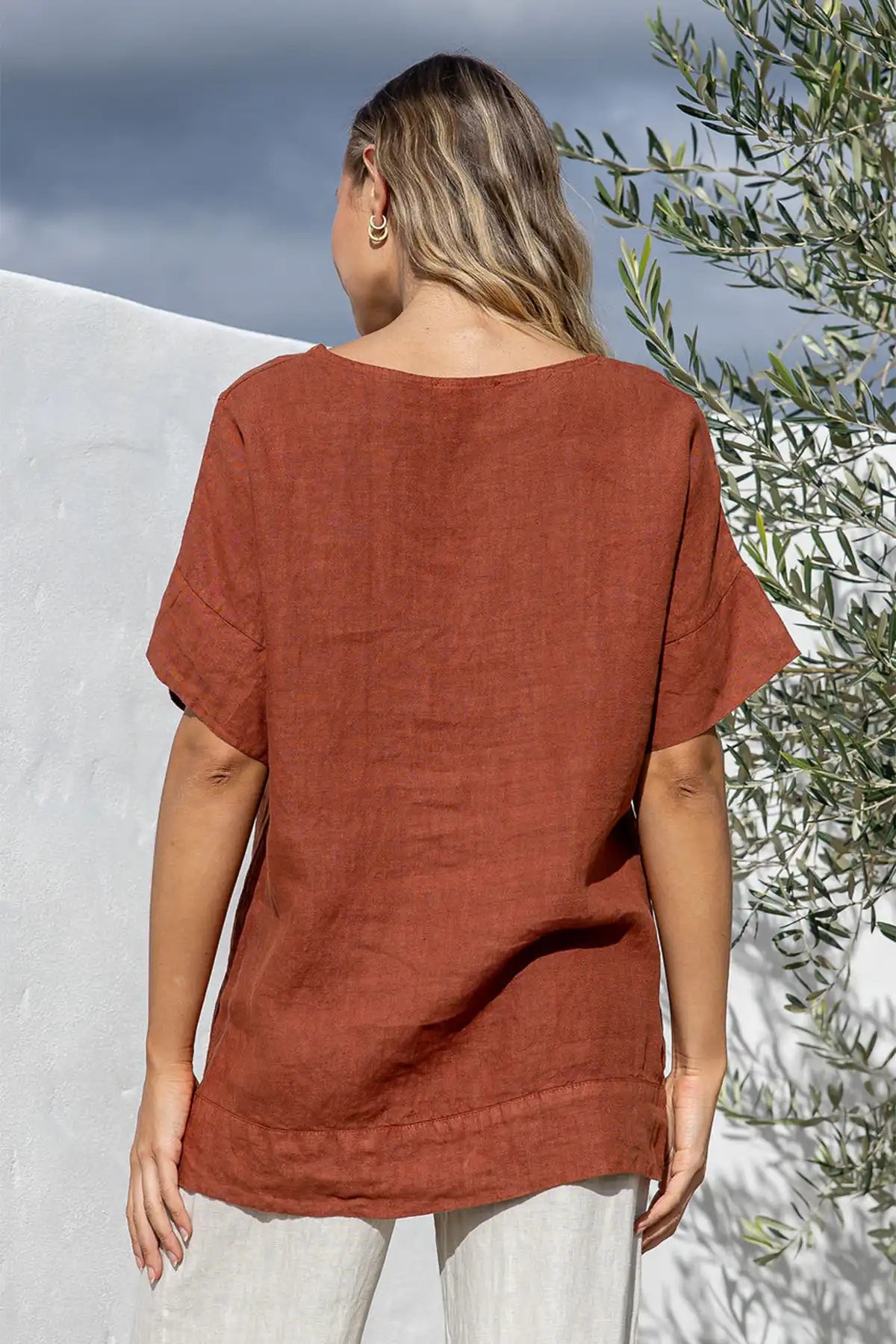 Person wearing a Valentina Italian Linen Coco Top with a white wall and olive tree in the background back view