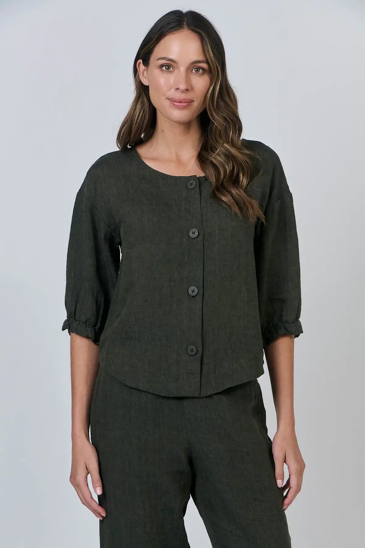 Woman wearing a dark green outfit with a buttoned top and pants on a light gray background