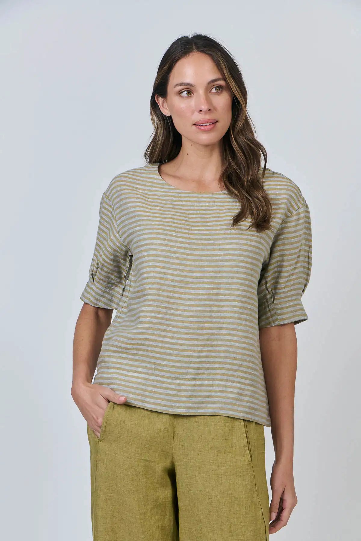 Woman wearing the Reed Stripe Linen Top and green pants against a plain background