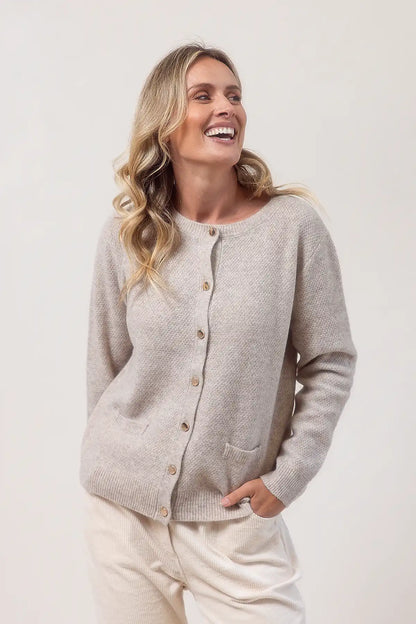 Woman wearing a merino wool wheat cardigan against a plain background