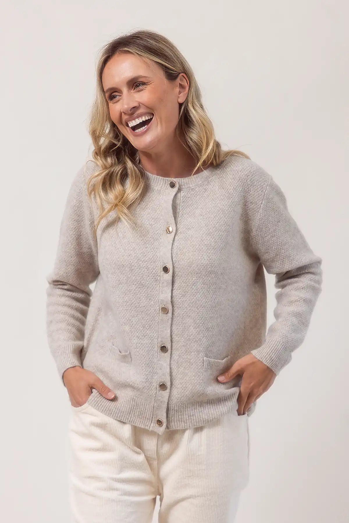 Woman wearing a light wheat cardigan with buttons on a white background