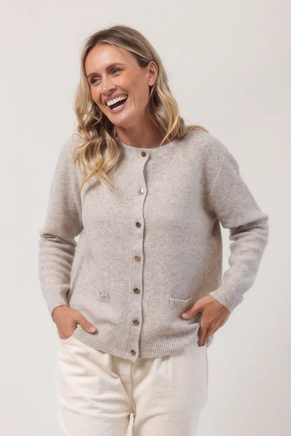 Woman wearing a light wheat cardigan with buttons on a white background