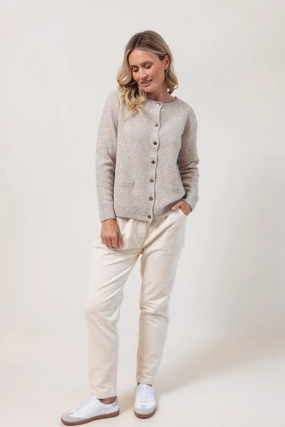 Woman wearing a wheat cardigan, white pants, and white sneakers on a plain background