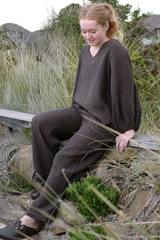 Woman sitting on a wooden bench in a natural setting with grass and rocks.