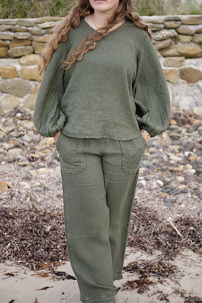 Person wearing an olive green outfit standing on a rocky beach.