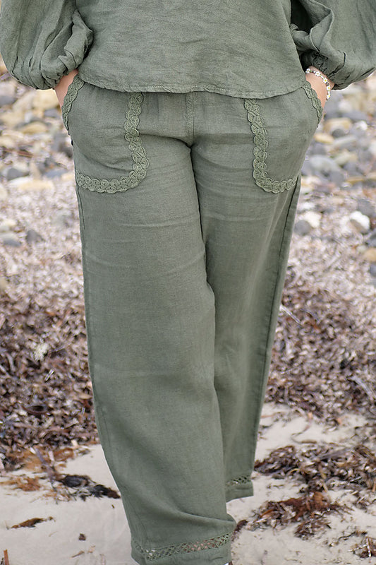 Person wearing olive green pants with lace trim on a beach.
