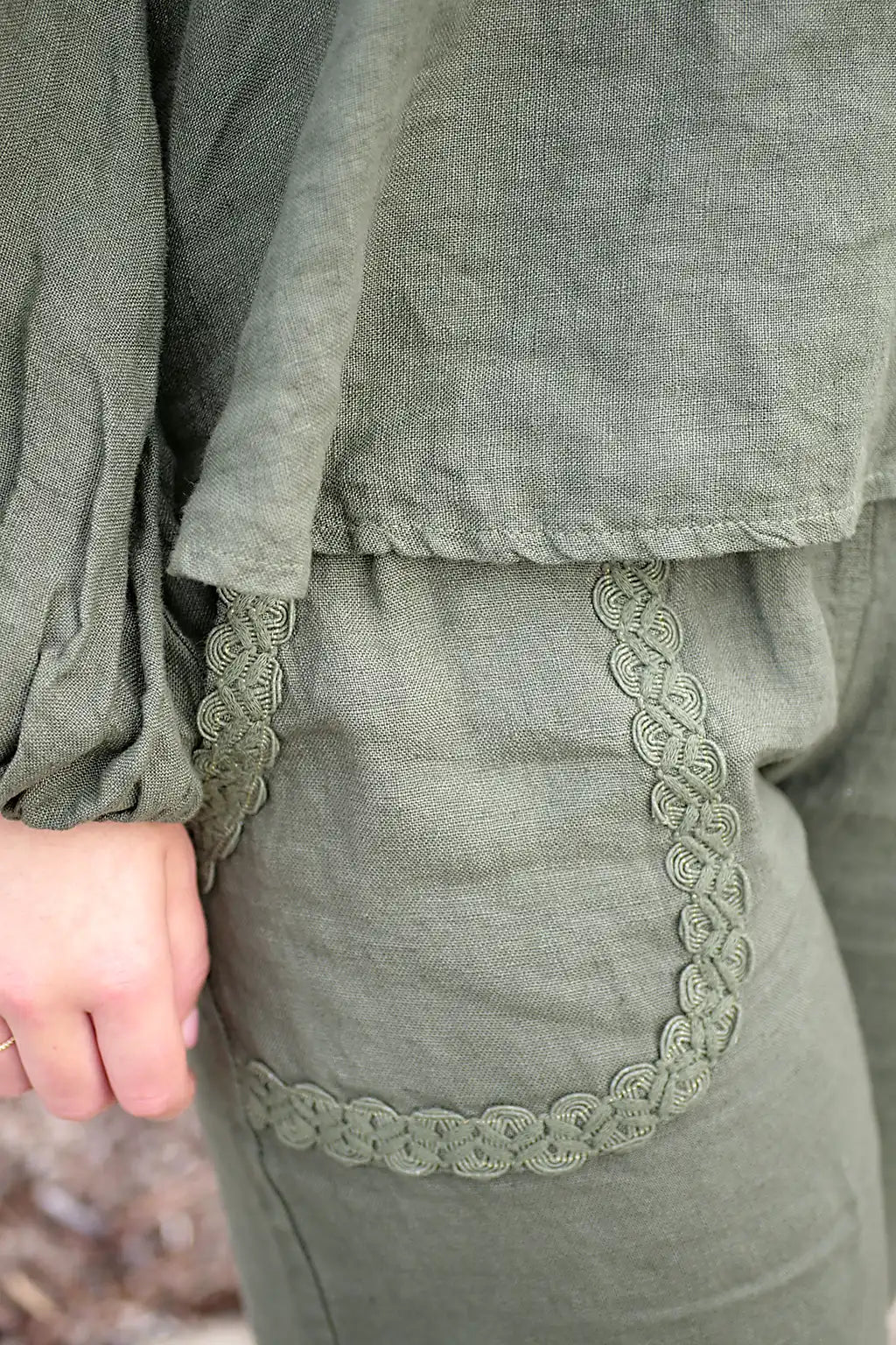 Green outfit with lace trim on front pocket and a blurred natural background