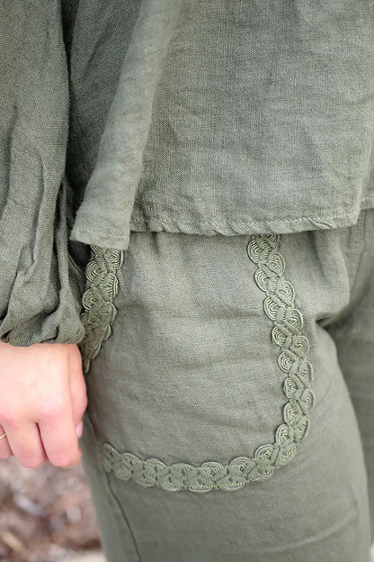 Green outfit with lace trim on front pocket and a blurred natural background