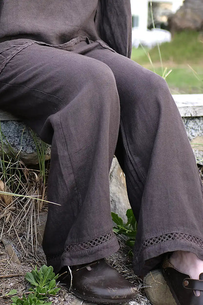 Person wearing dark brown pants sitting on a stone ledge with grass and plants around.