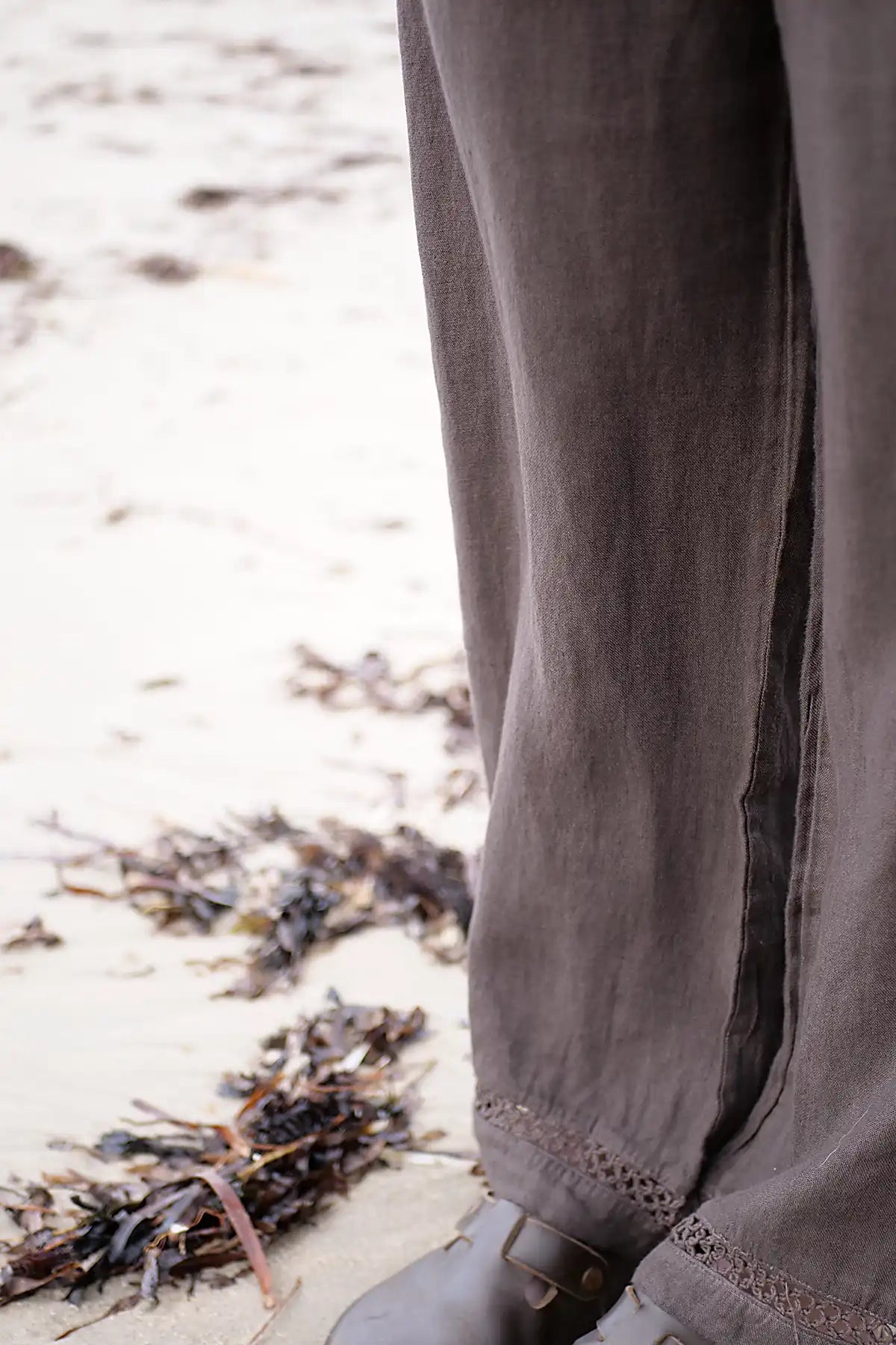 Close-up of chocolate brown pants on a sandy surface with seaweed.