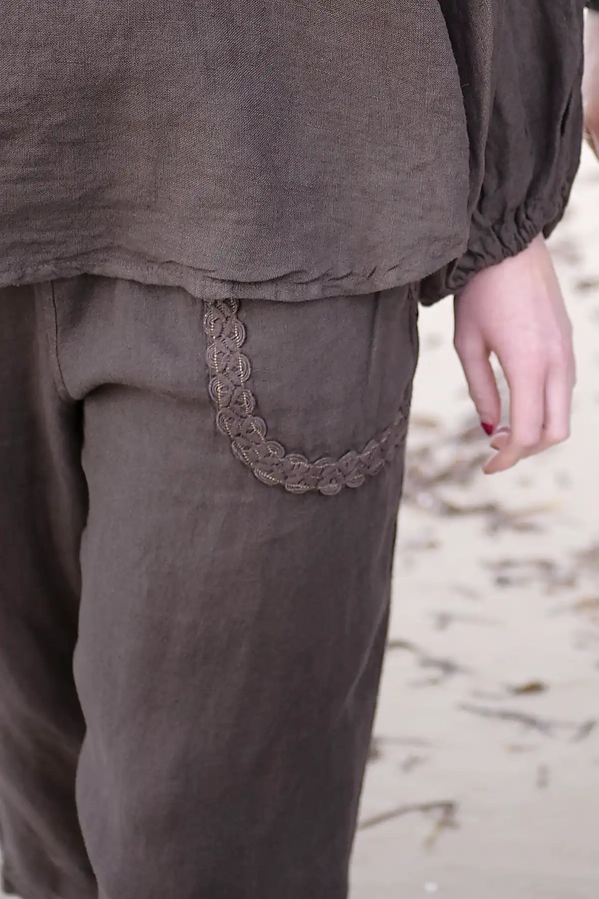 Brown pants with a decorative pocket trim on a blurred natural background