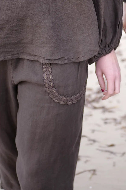 Brown pants with a decorative pocket trim on a blurred natural background