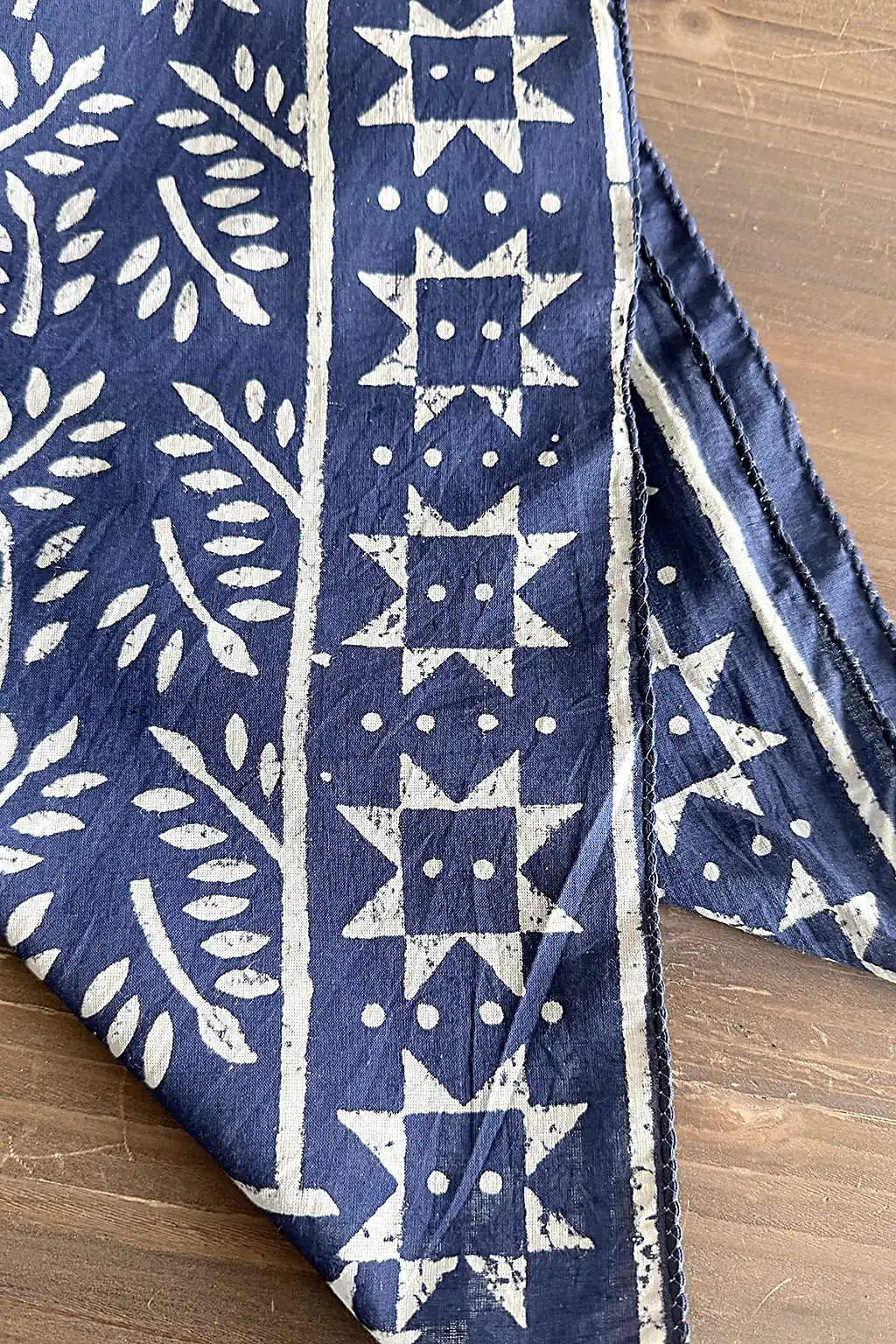 Blue cotton fabric scarf with white geometric patterns on a wooden surface