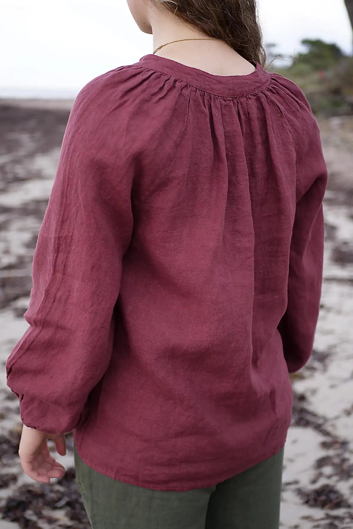 Person wearing a berry long-sleeve top on a beach.