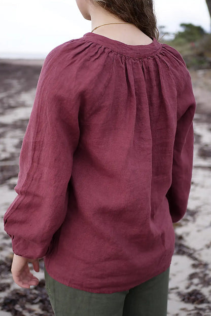 Person wearing a berry long-sleeve top on a beach.