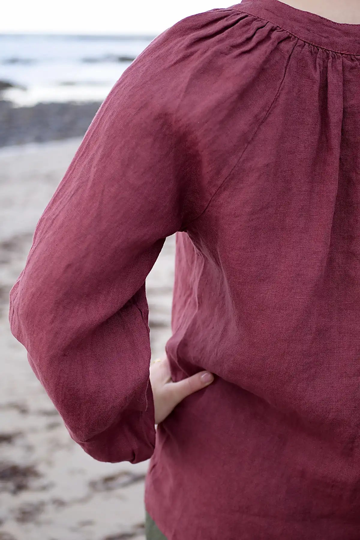 Close-up of a woman wearing a berry long-sleeve top on a beach.